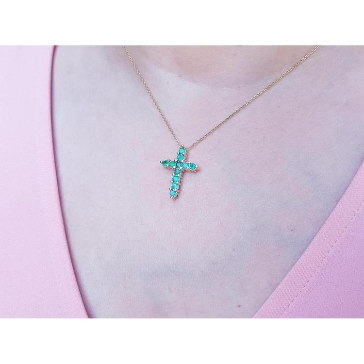 14K yellow gold cross pendant necklace with eleven round-cut Colombian emeralds on a woman's neck.