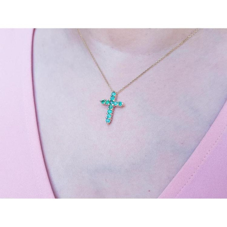 14K yellow gold cross pendant necklace with eleven round-cut Colombian emeralds on a woman's neck.