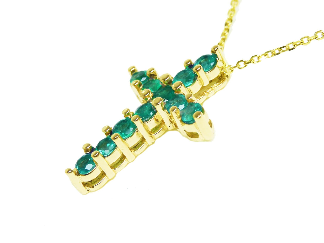 Gold cross pendant with emerald stones on a side position top and gallery are visibles.