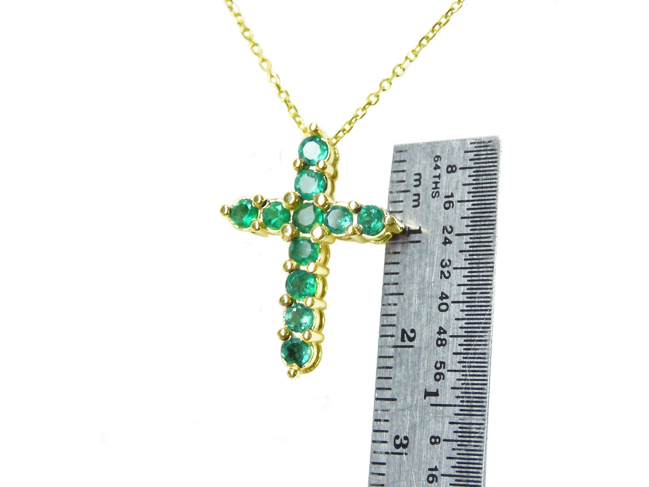 Natural emerald cross necklace next to a ruler on a white background.