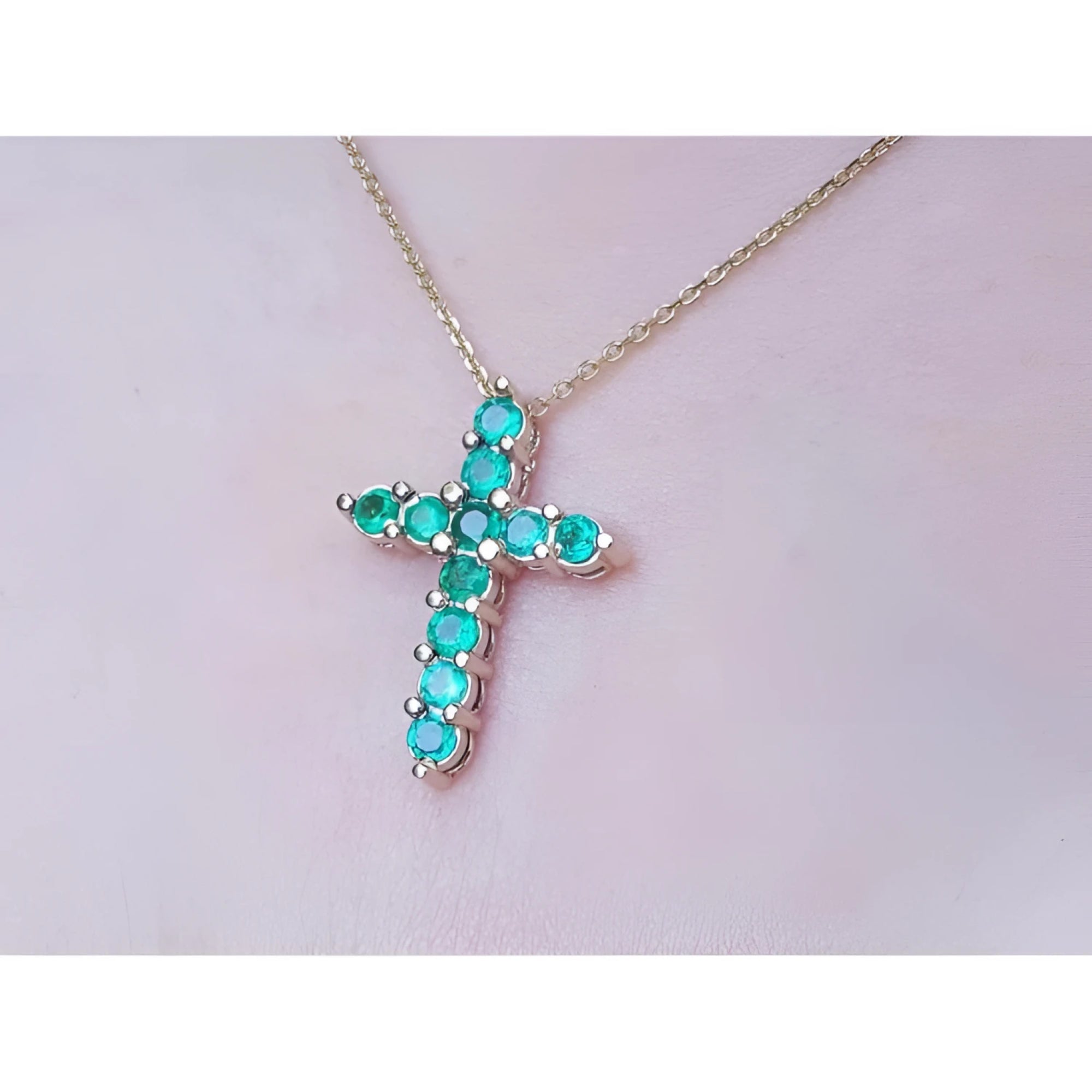 Cross-shaped necklace with natural emeralds on a light pink skin background.