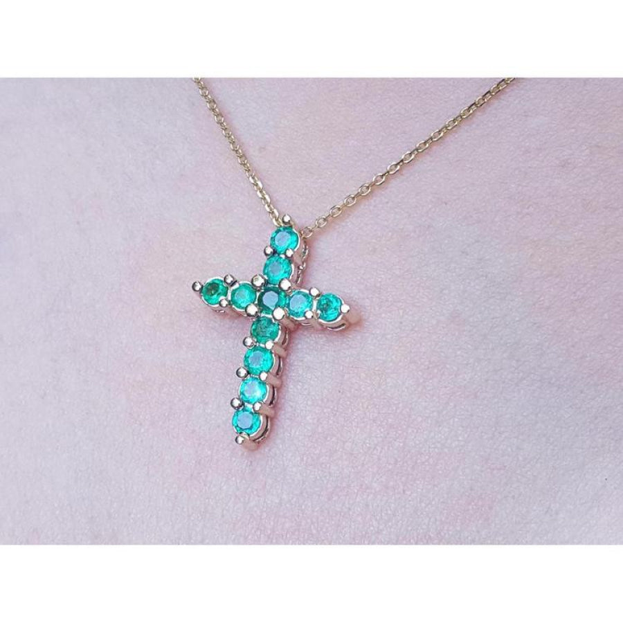 Cross-shaped necklace with natural emeralds on a light pink skin background.