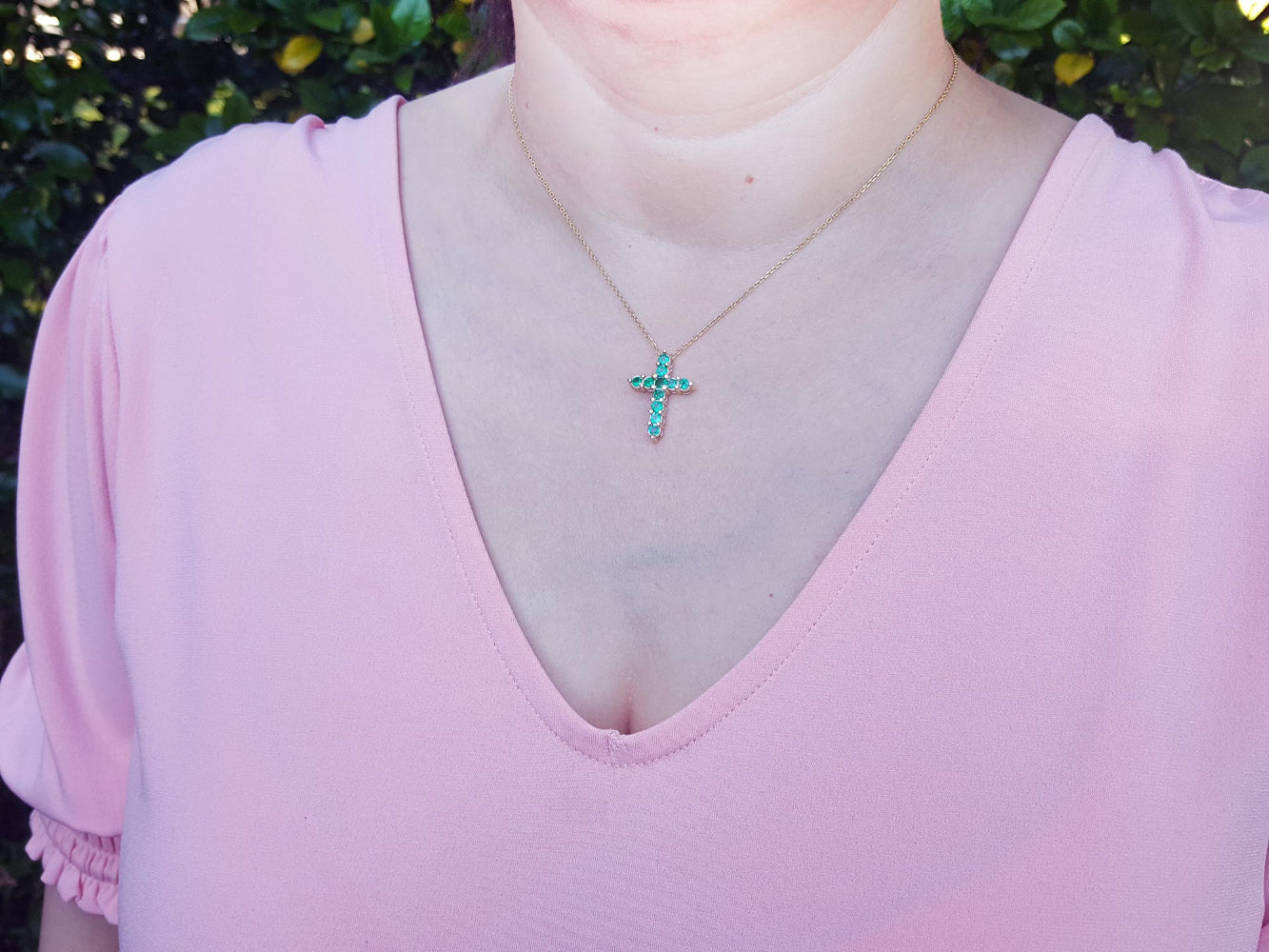 A woman wearing a pink top with a necklace featuring an emerald cross pendant.