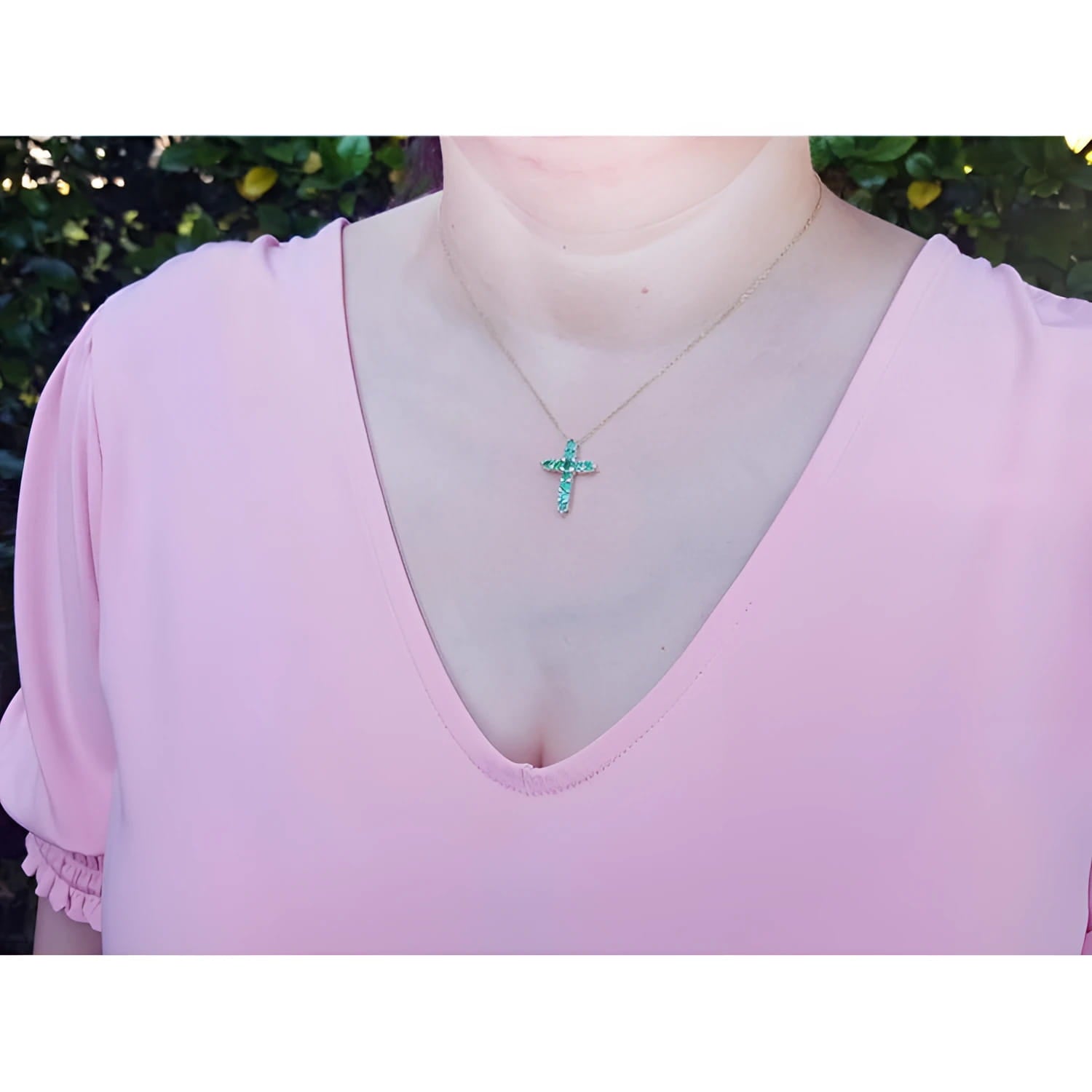 14K yellow gold cross pendant necklace with eleven round-cut Colombian emeralds on a woman's neck.