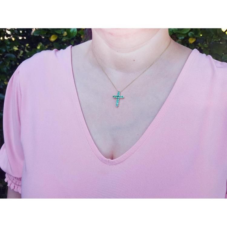 14K yellow gold cross pendant necklace with eleven round-cut Colombian emeralds on a woman's neck.