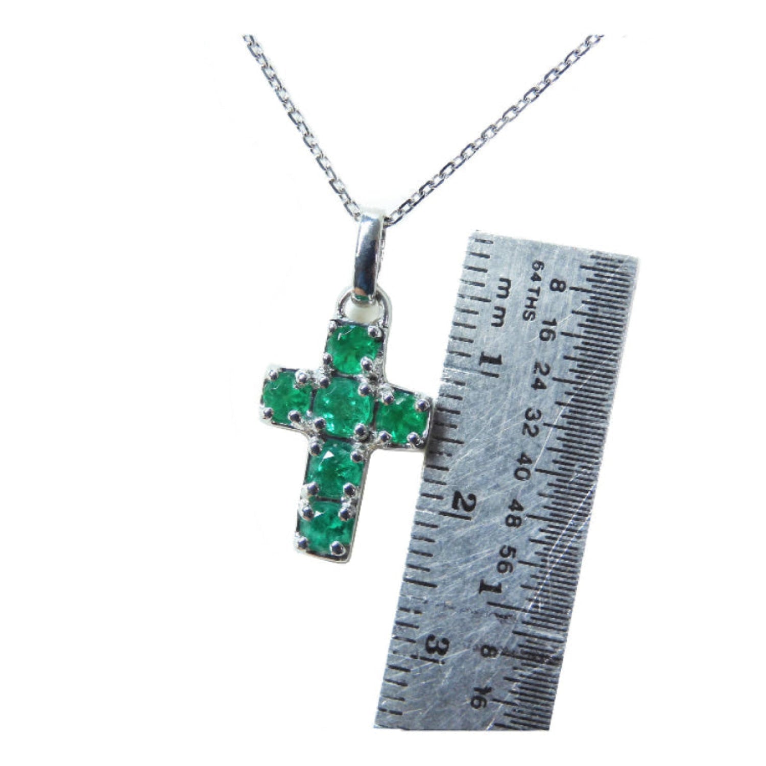 Cross-shaped pendant with round cut natural colombian emeralds on a chain, next to a ruler for scale.