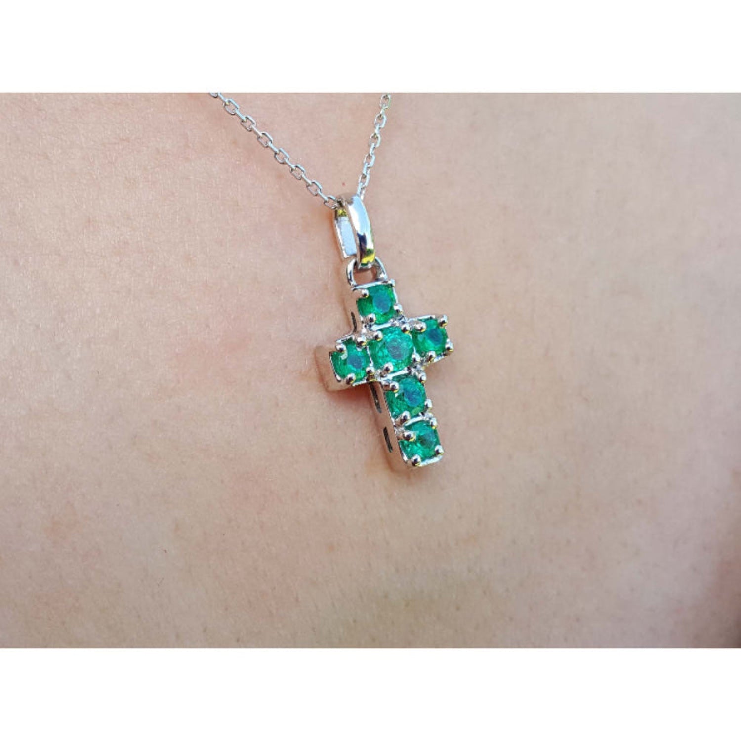 A 14k white gold cross pendant round   cut natural colombian emeralds on a chain, worn on skin.