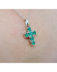 A 14k white gold cross pendant round   cut natural colombian emeralds on a chain, worn on skin.