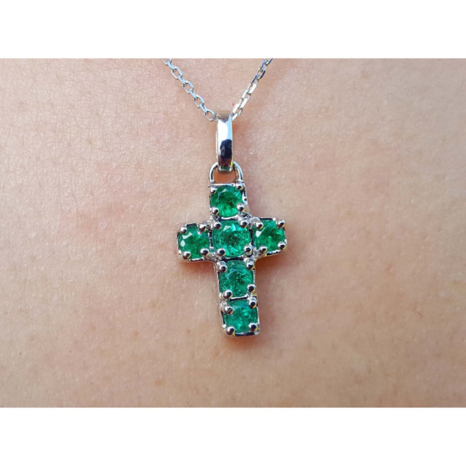 Cross-shaped natural emerald pendant on a chain, worn on skin.