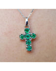 Cross-shaped natural emerald pendant on a chain, worn on skin.