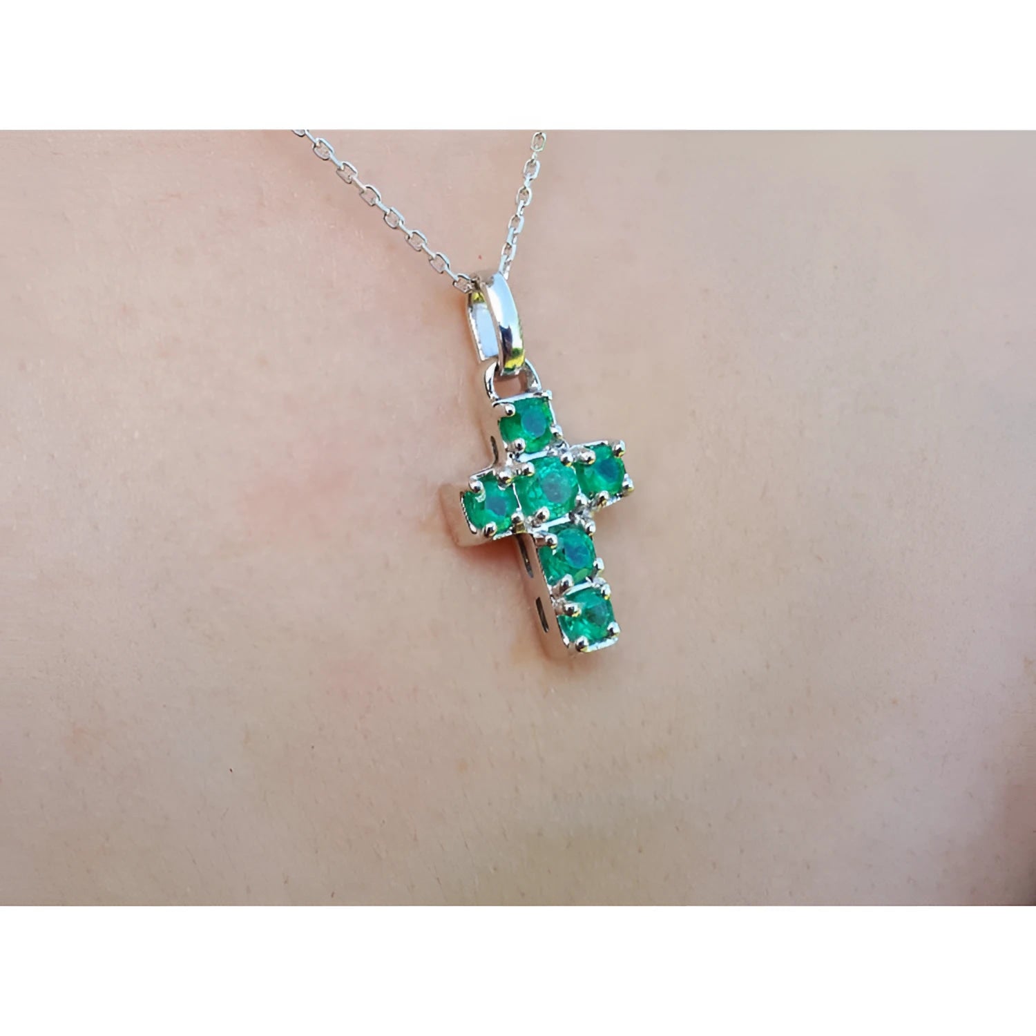 A 14k white gold cross pendant round   cut natural colombian emeralds on a chain, worn on skin.