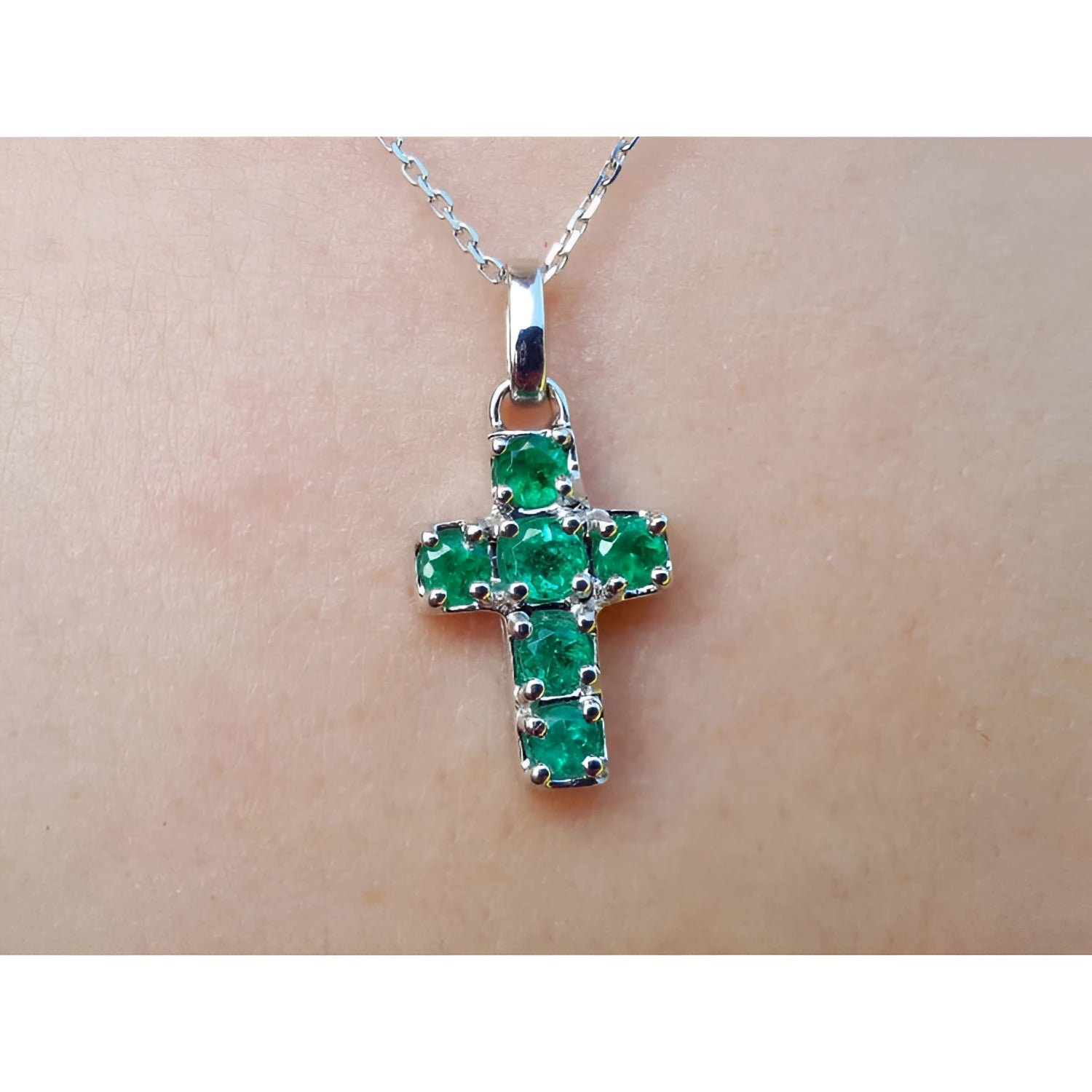Cross-shaped natural emerald pendant on a chain, worn on skin.