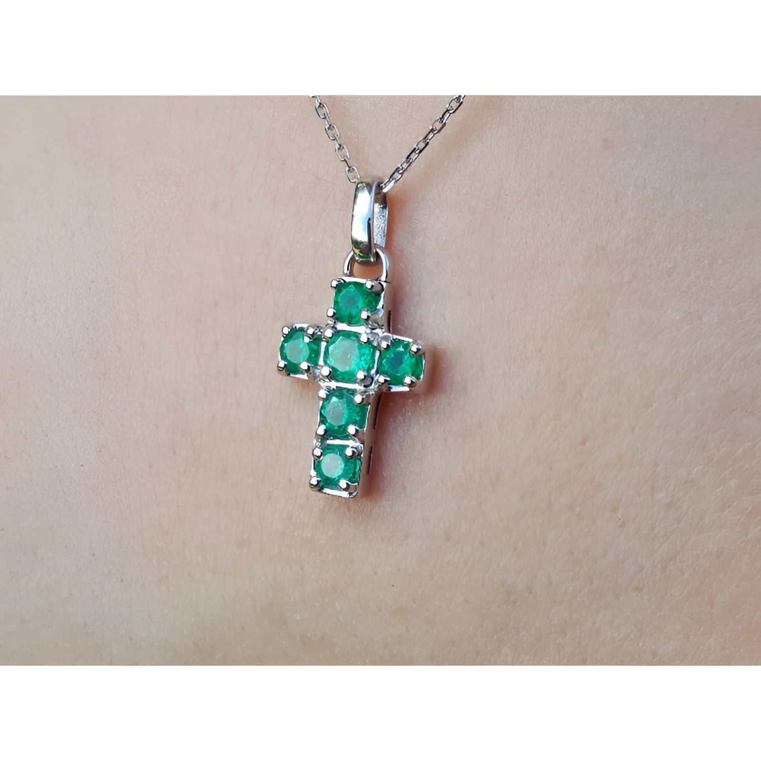 A 14k white gold genuine emerald cross pendant on a chain against a skin background.