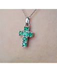 A 14k white gold genuine emerald cross pendant on a chain against a skin background.