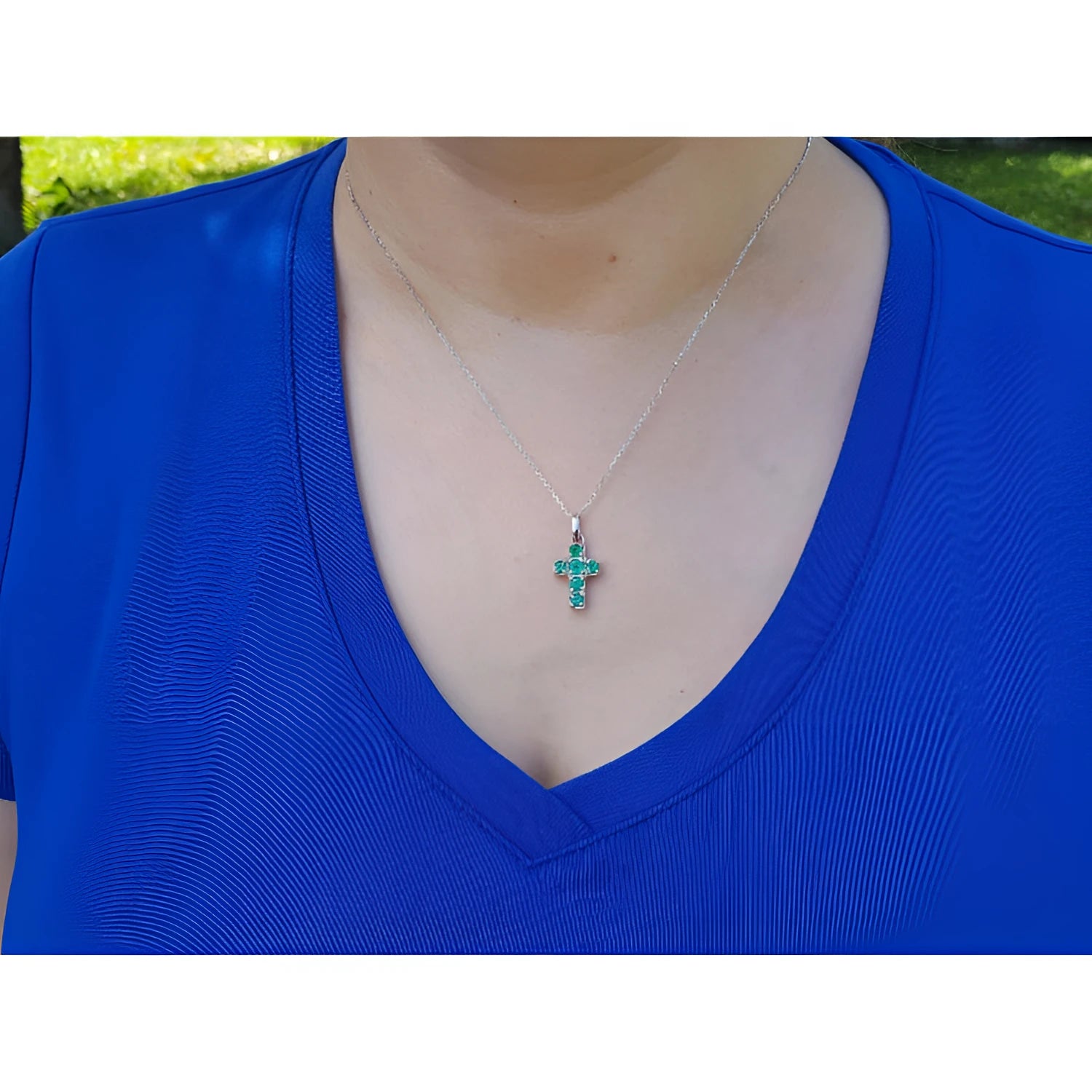 A women wearing a blue shirt with a white gold necklace featuring a colombian emerald cross pendant.