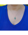 A women wearing a blue shirt with a white gold necklace featuring a colombian emerald cross pendant.