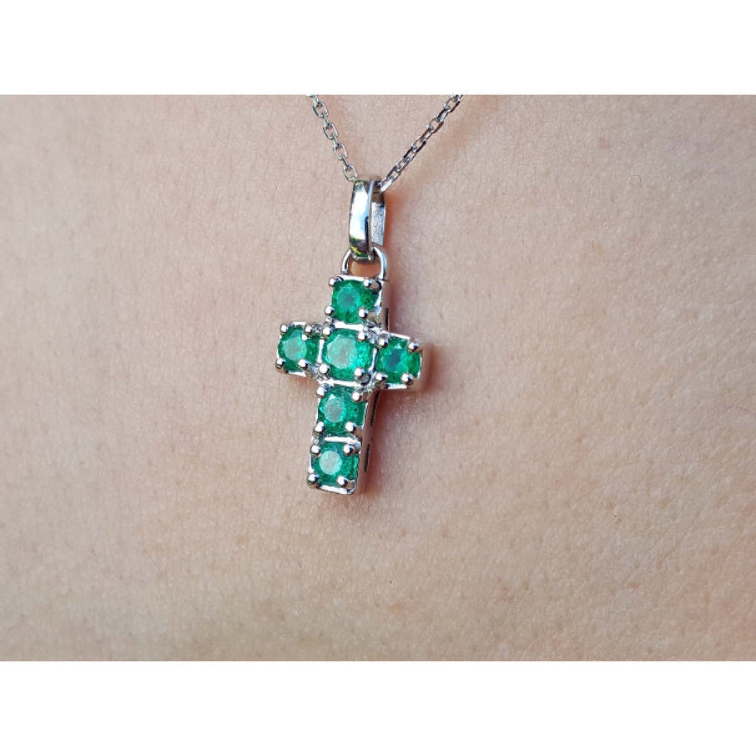 A 14k white gold genuine emerald cross pendant on a chain against a skin background.