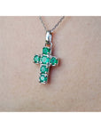 A 14k white gold genuine emerald cross pendant on a chain against a skin background.
