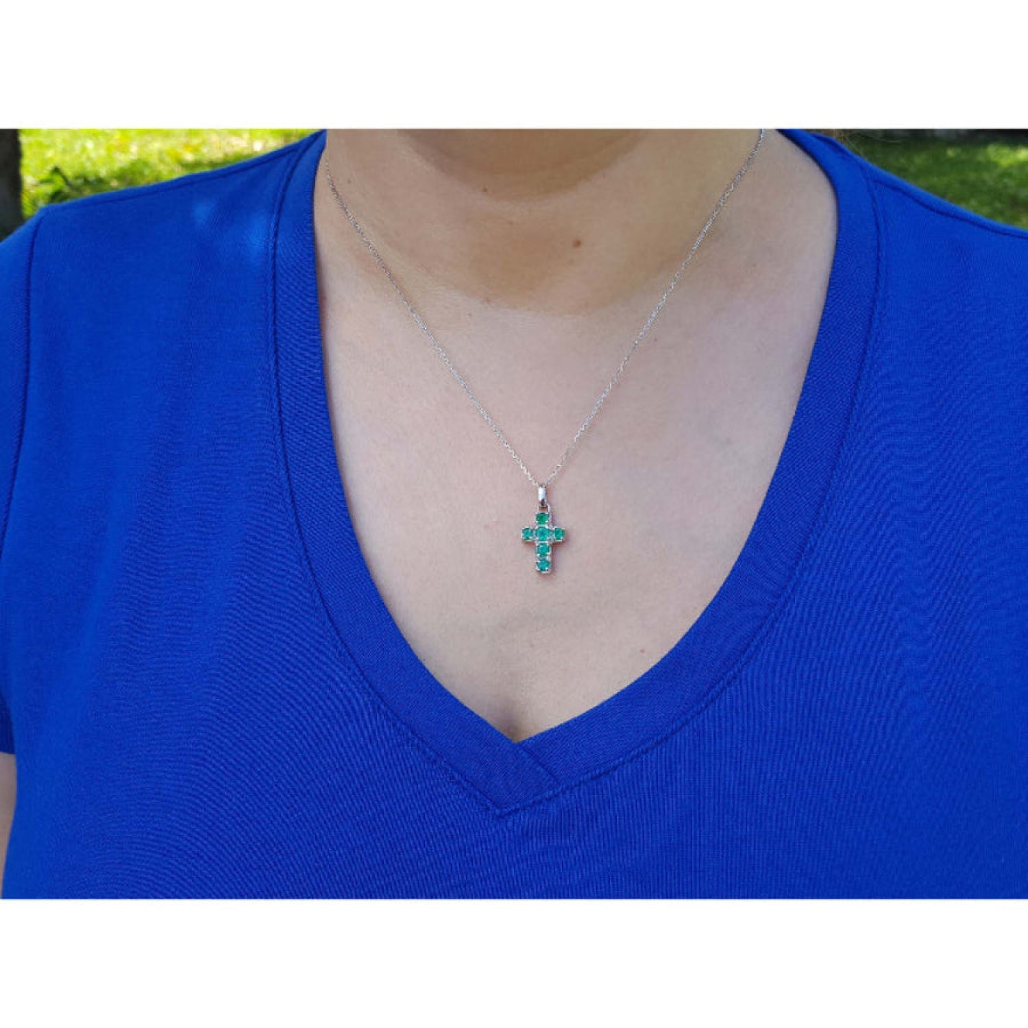 A women wearing a blue shirt with a white gold necklace featuring a colombian emerald cross pendant.