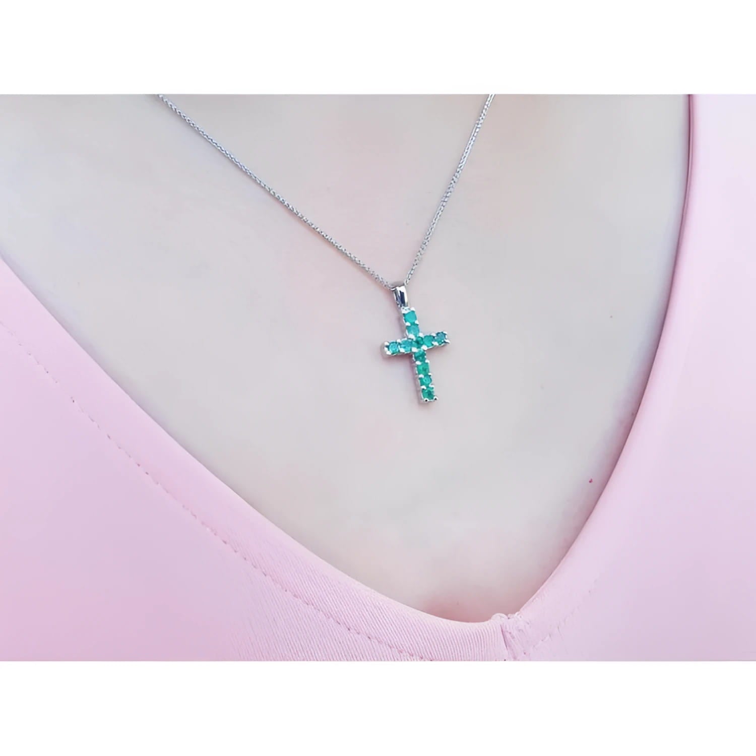 Emerald cross pendant necklace with round-cut emeralds in 18K white gold, worn on a pink top.