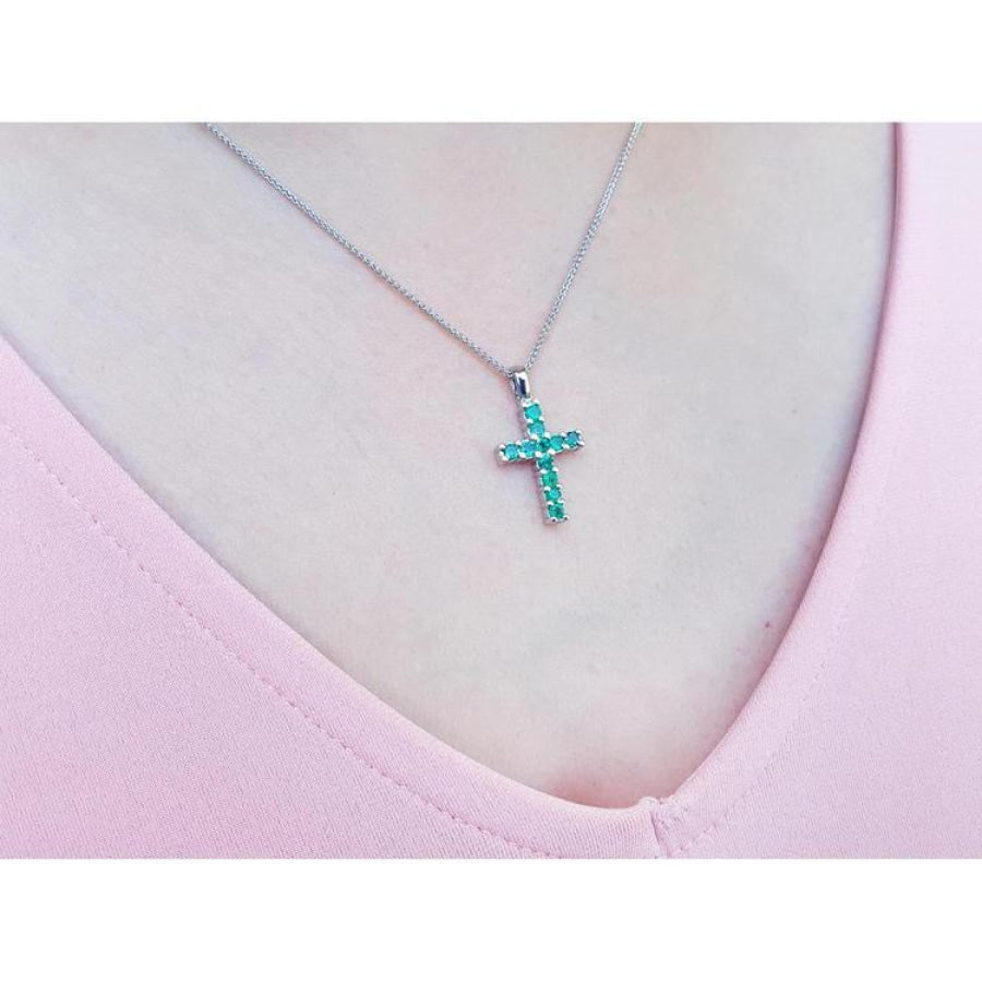 Emerald cross pendant necklace with round-cut emeralds in 18K white gold, worn on a pink top.