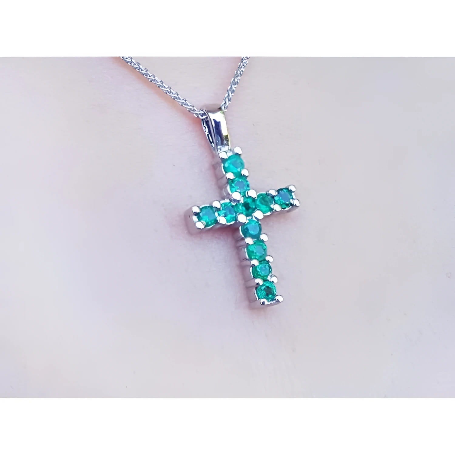 18K white gold cross pendant with round-cut emeralds on a delicate chain, worn on a person.