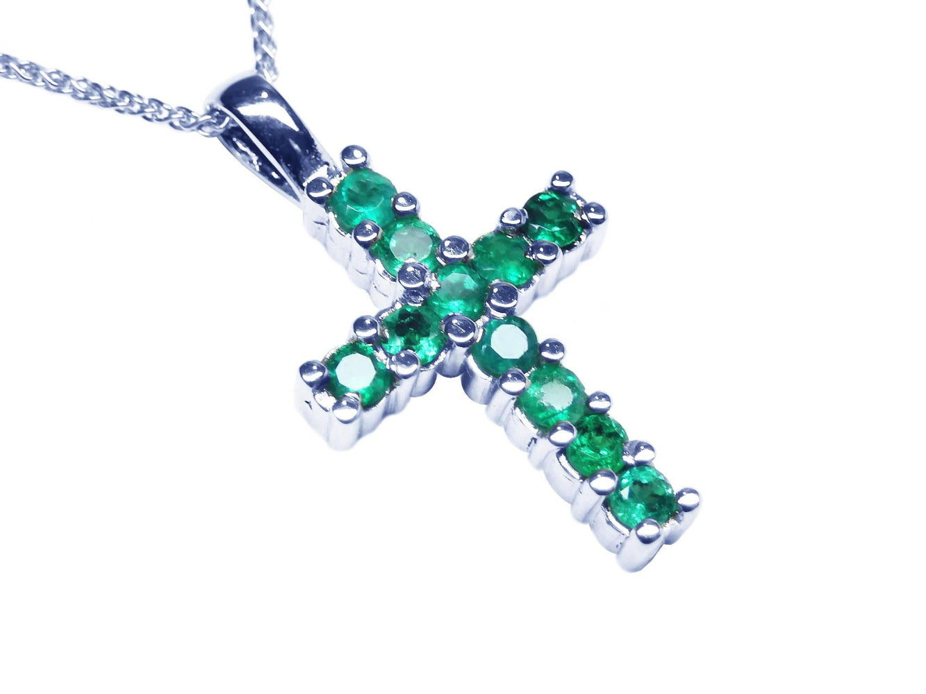 A 18k white gold cross pendant with round cut Colombian emeralds on a topside view position.