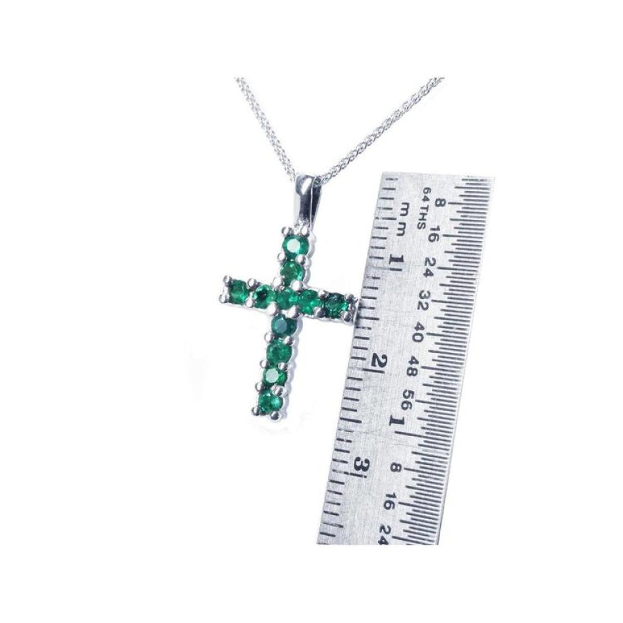 Round-cut emerald cross pendant necklace in 18K white gold, shown with a ruler for size.