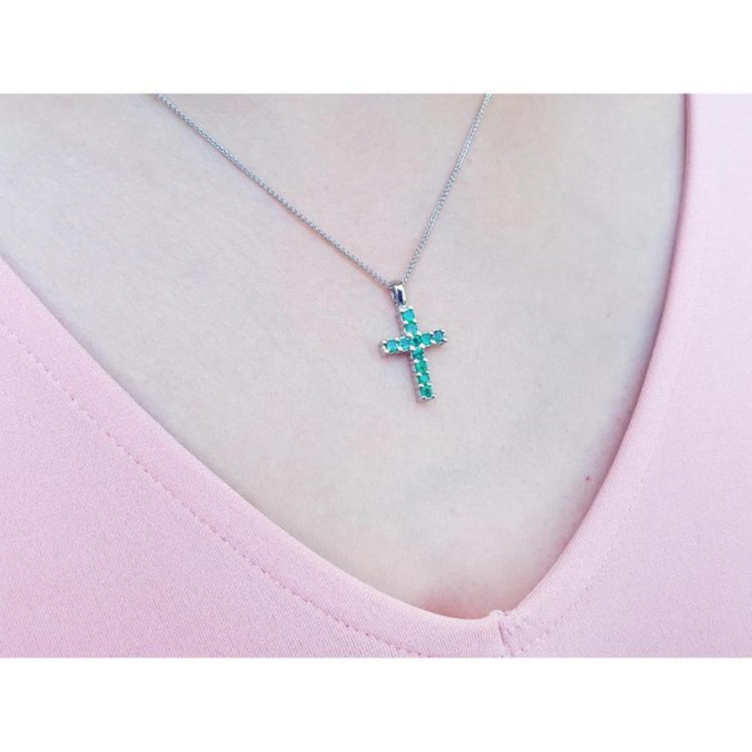 Emerald cross pendant necklace with round-cut emeralds in 18K white gold, worn on a pink top.