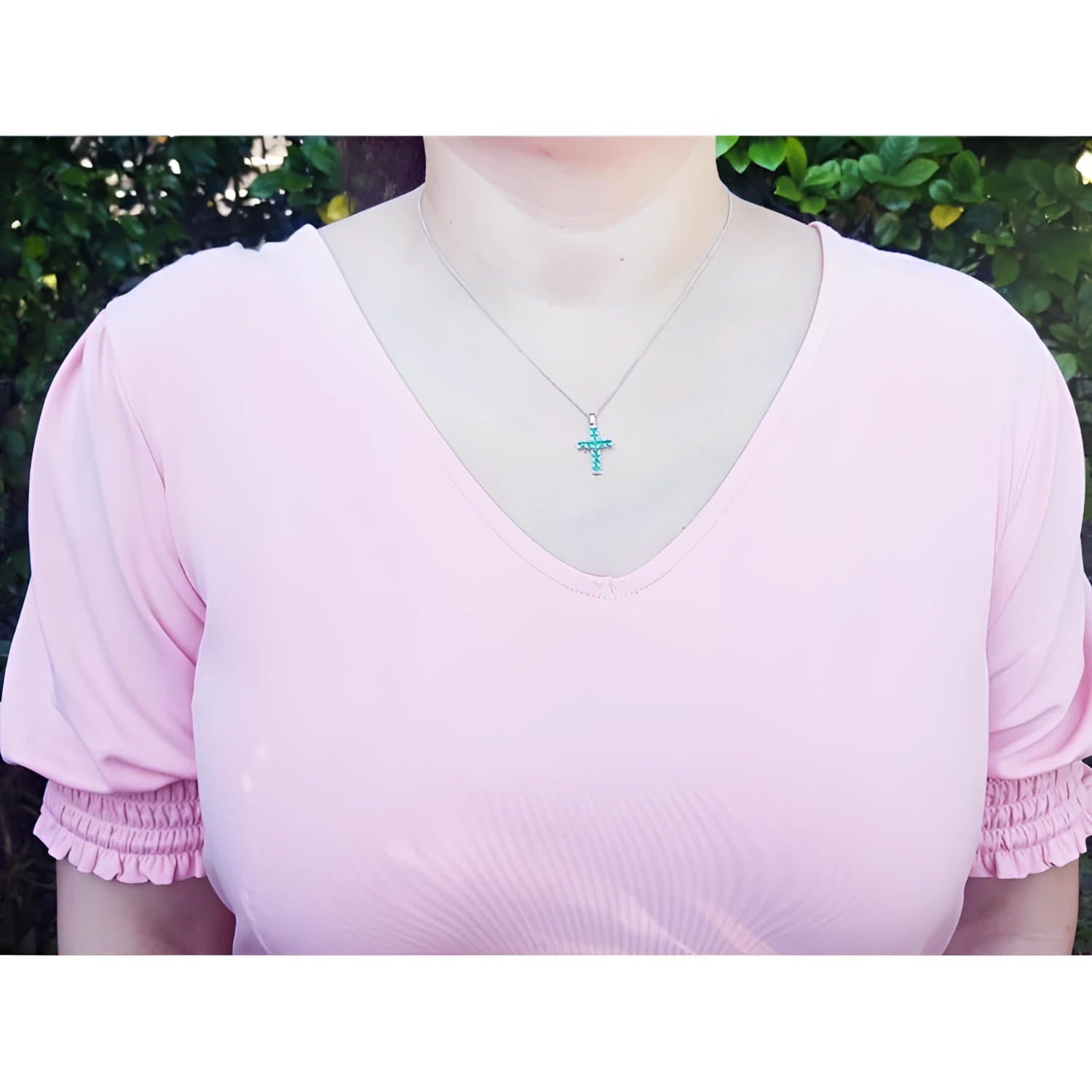 Woman wearing a small round-cut emerald cross pendant necklace on an 18K white gold chain.