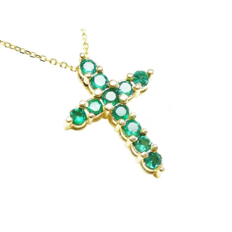 A cross pendant on a right-side position and top view of eleven round cut emeralds prong set in yellow gold.