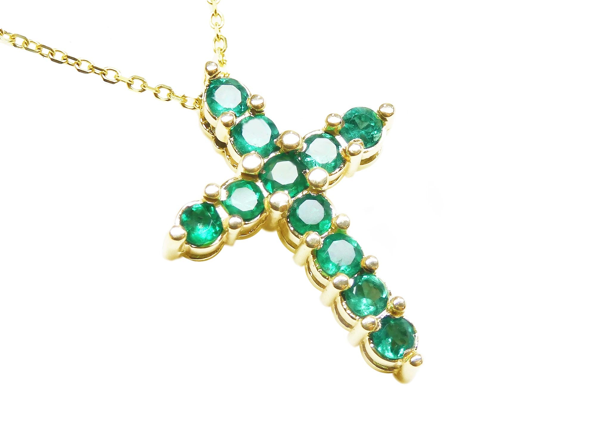 A cross pendant on a right-side position and top view of eleven round cut emeralds prong set in yellow gold