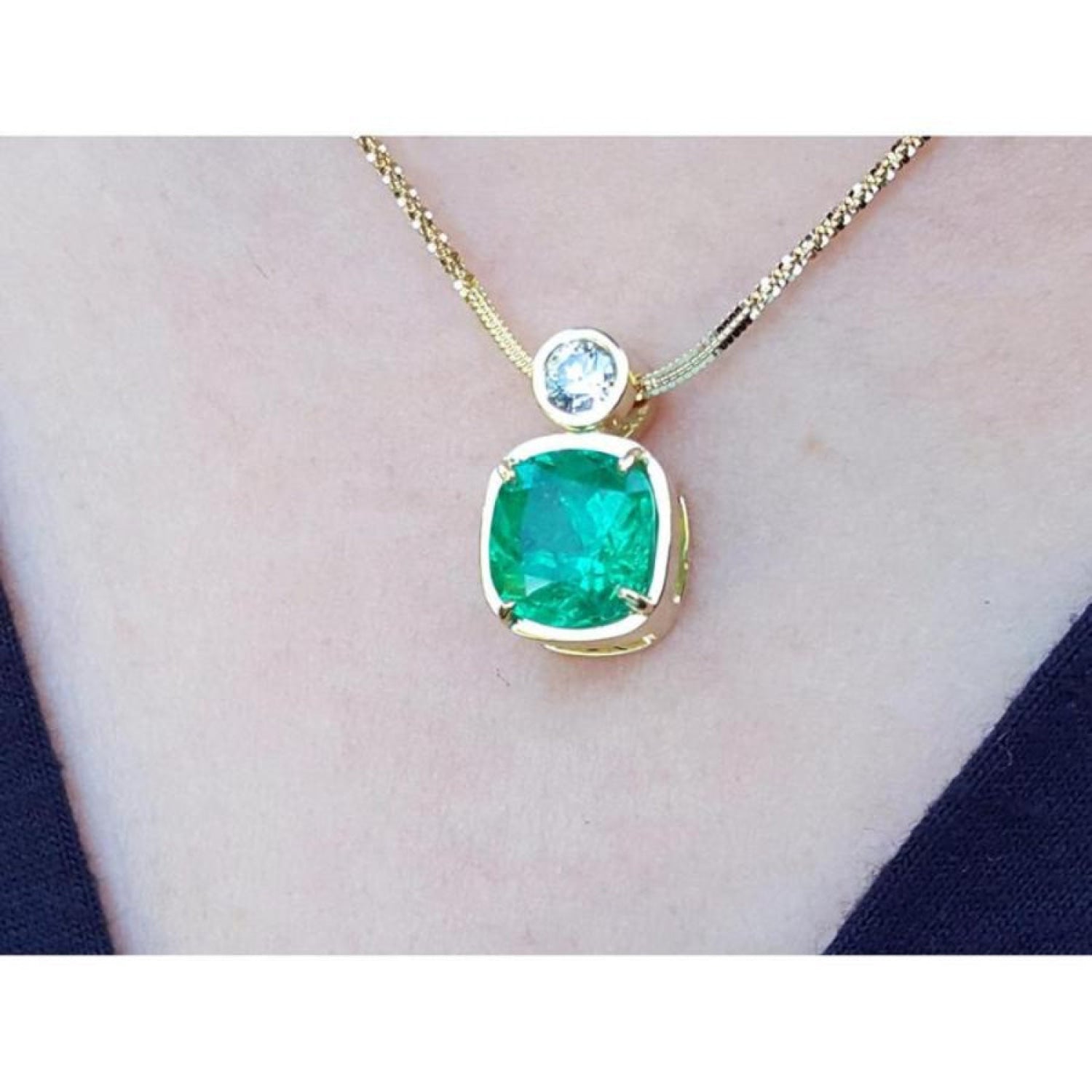 18k gold necklace with a cushion cut emerald pendant on a person's neck.