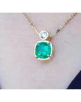 18k gold necklace with a cushion cut emerald pendant on a person's neck.