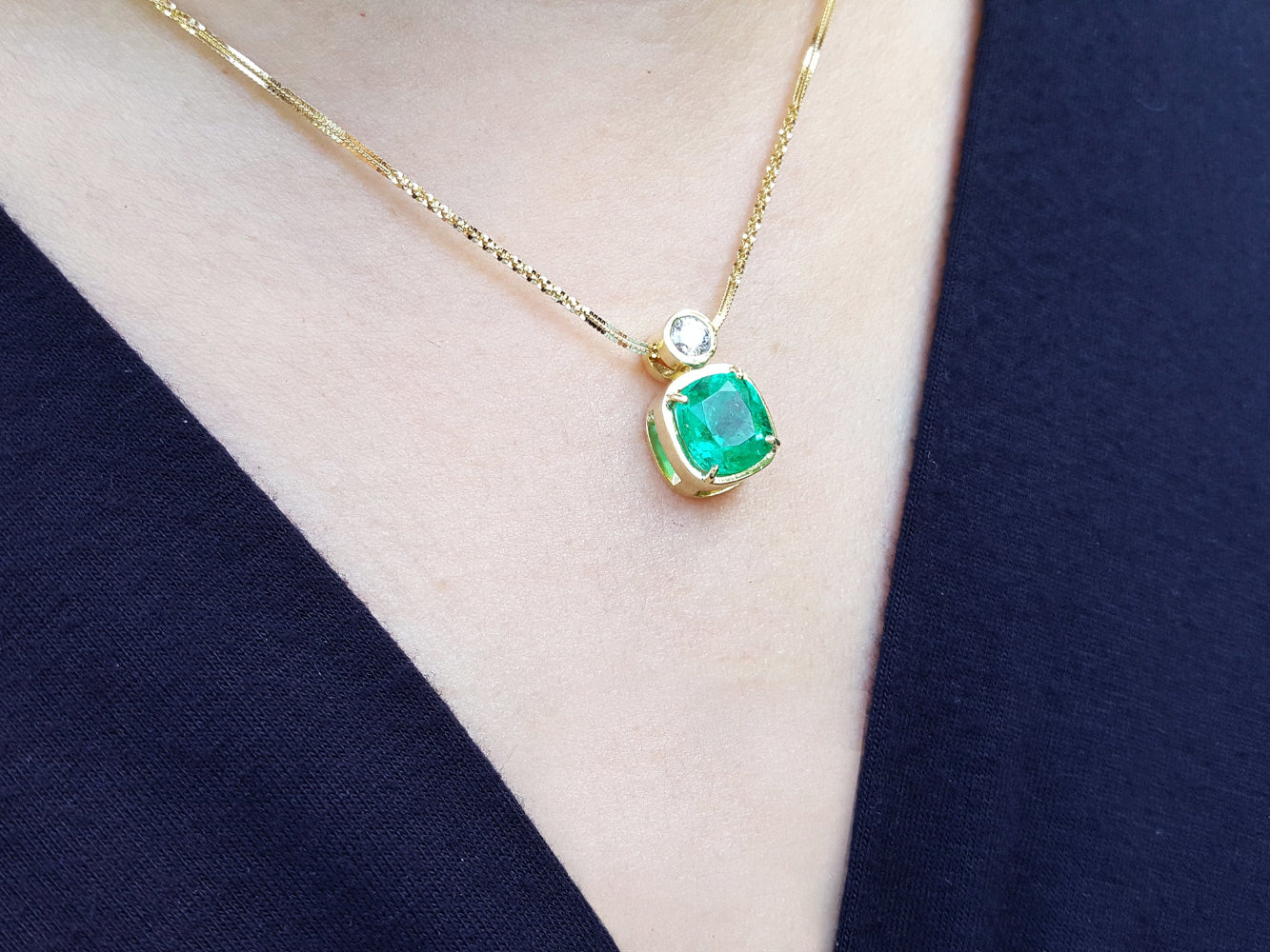 Gold necklace with a natural emerald pendant on a person wearing a navy-blue top.