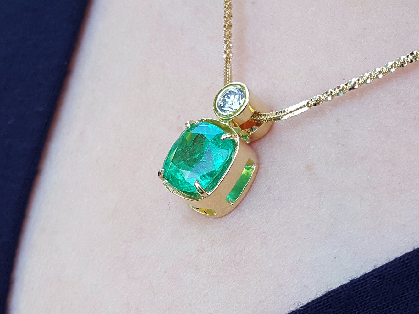 A yellow gold necklace with a cushion emerald pendant on a skin background