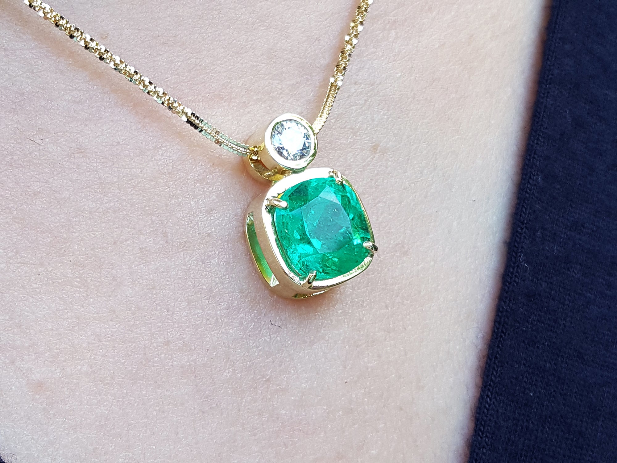 Gold necklace with a cushion cut emerald pendant on a person&#39;s neck