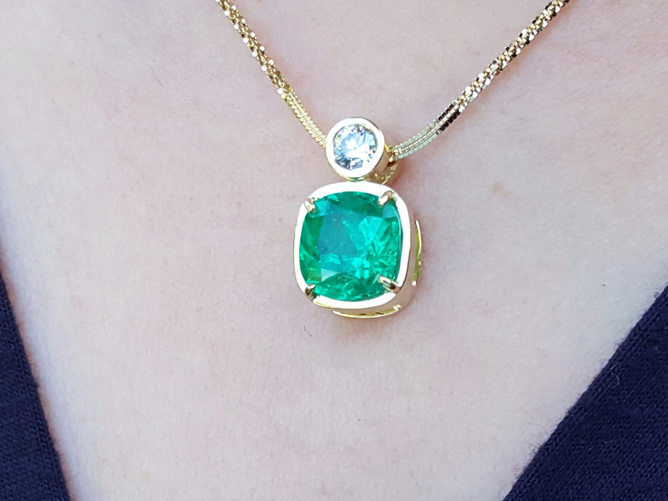 Gold necklace with a cushion cut emerald pendant on a person's neck