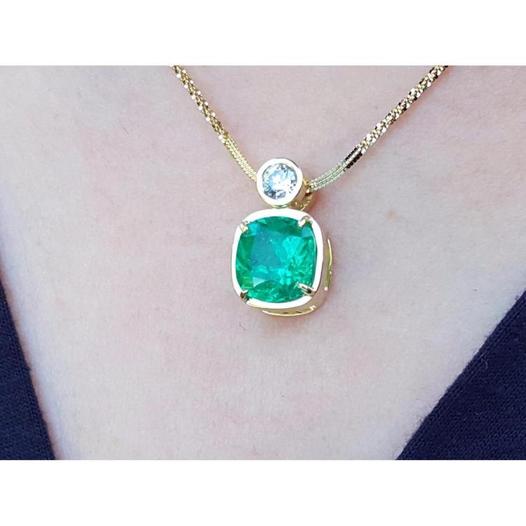 Gold necklace with a cushion cut emerald pendant on a person's neck