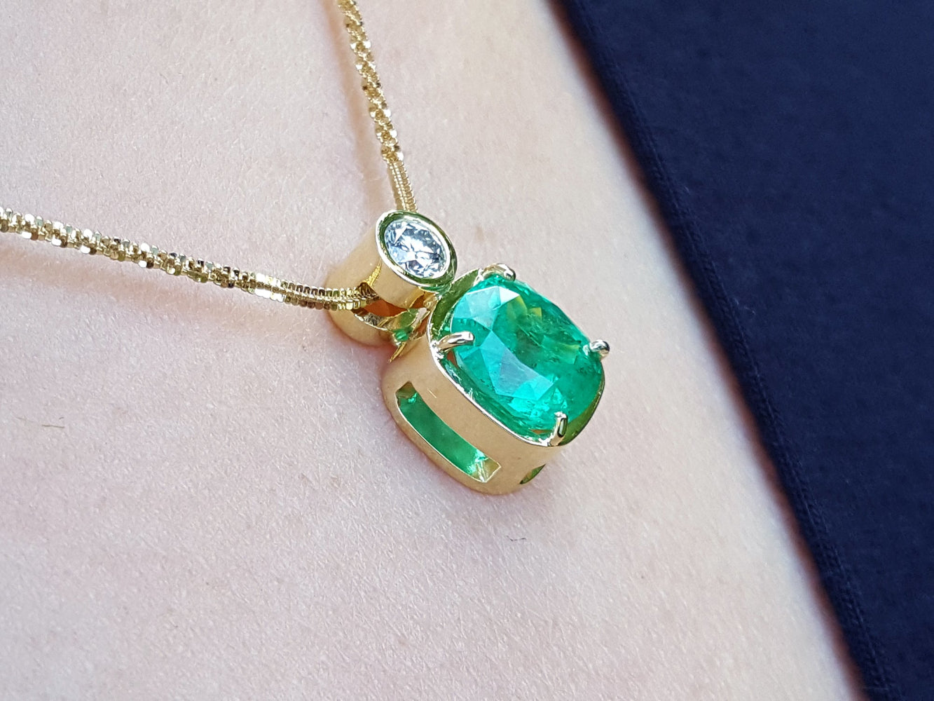 Gold necklace with a natural emerald pendant on a soft fabric background