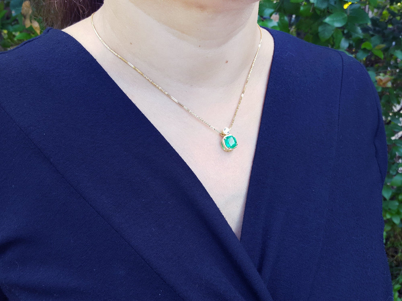 Person wearing a gold necklace with an emerald pendant against a blurred green background