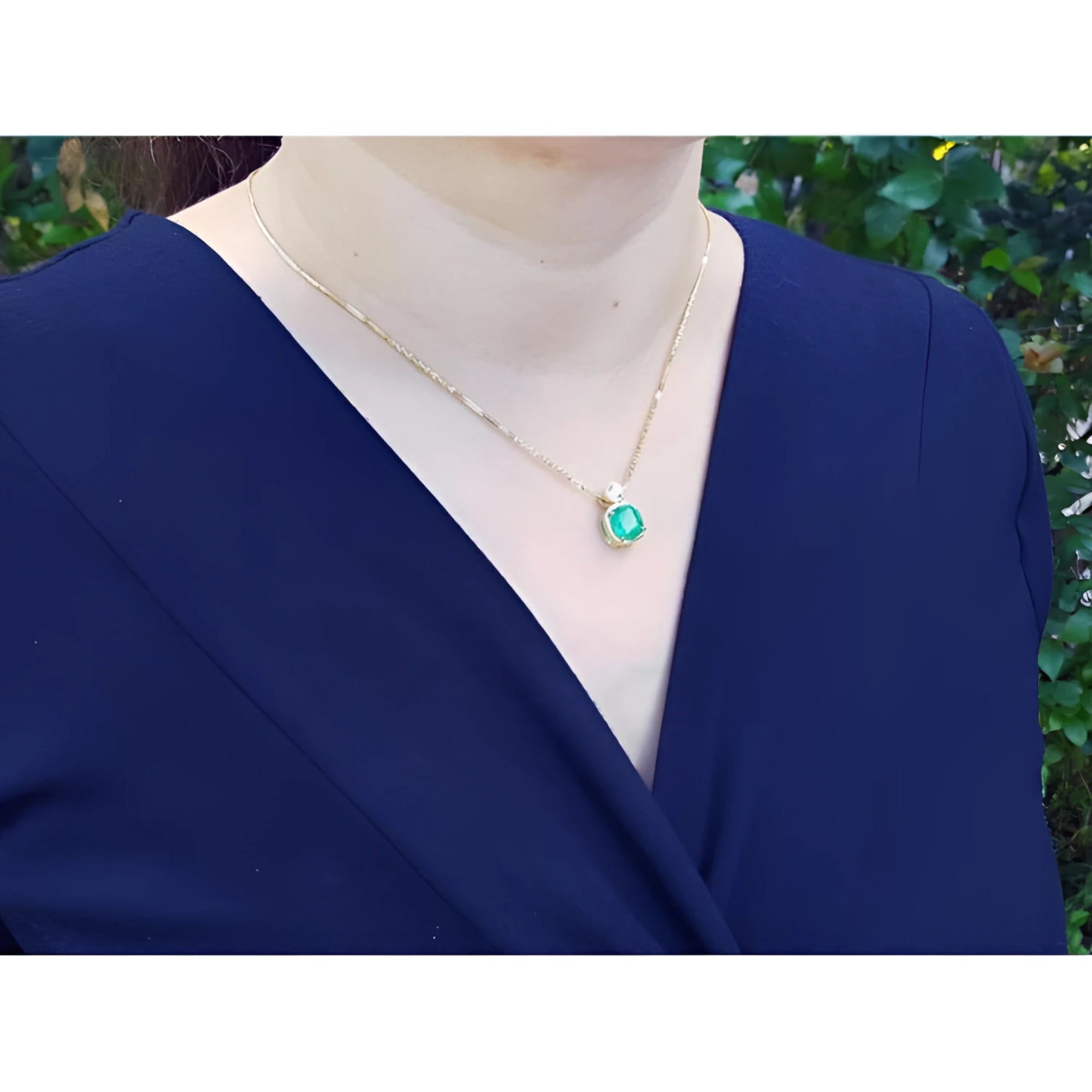 Woman wearing a vibrant deep bluish-green emerald cushion cut pendant in 18K yellow gold.