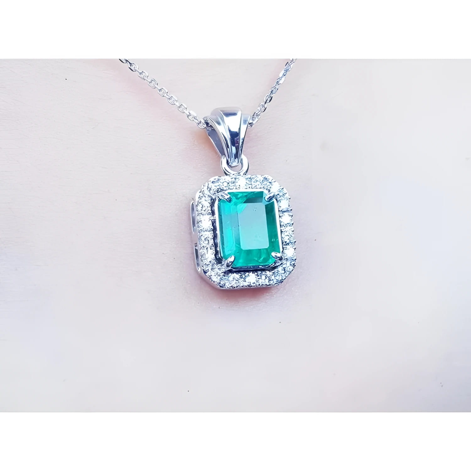 Emerald-cut emerald pendant with halo diamonds in 14K white gold on a delicate chain.