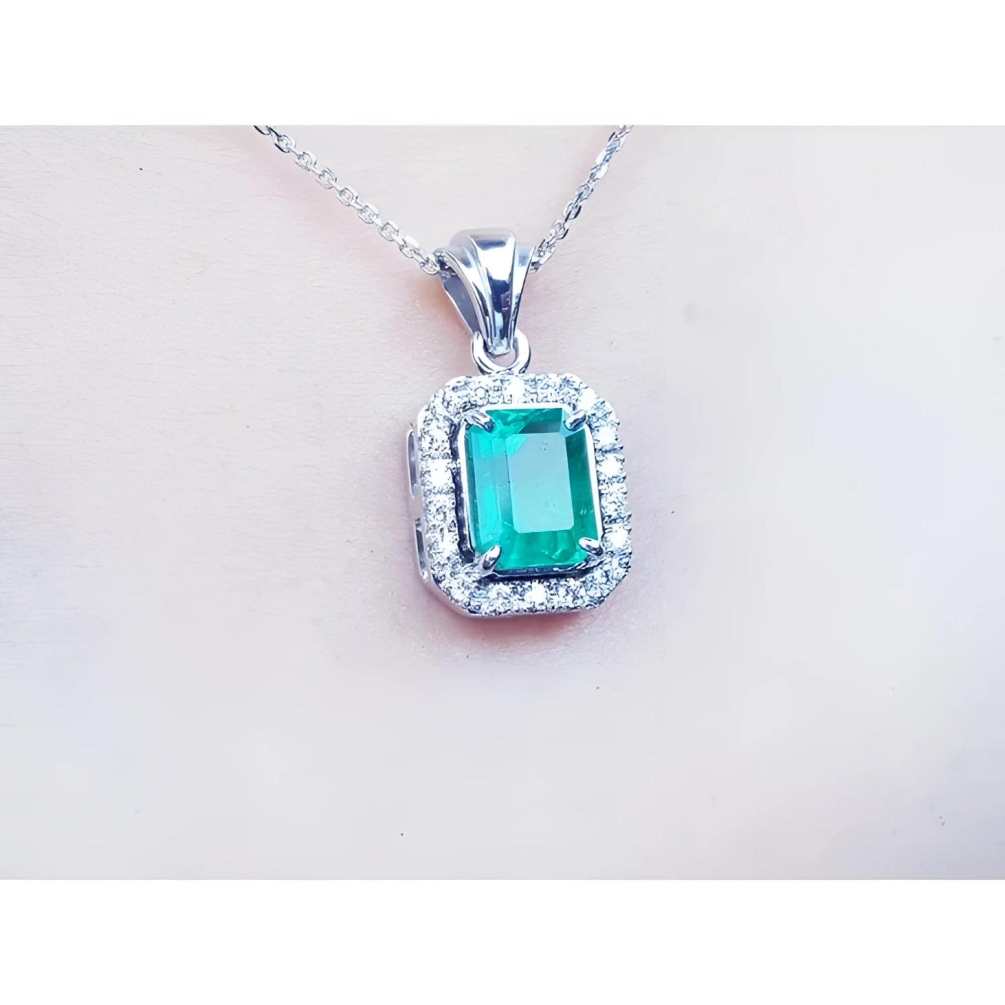 Emerald-cut emerald pendant with halo diamonds in 14K white gold on a delicate chain.
