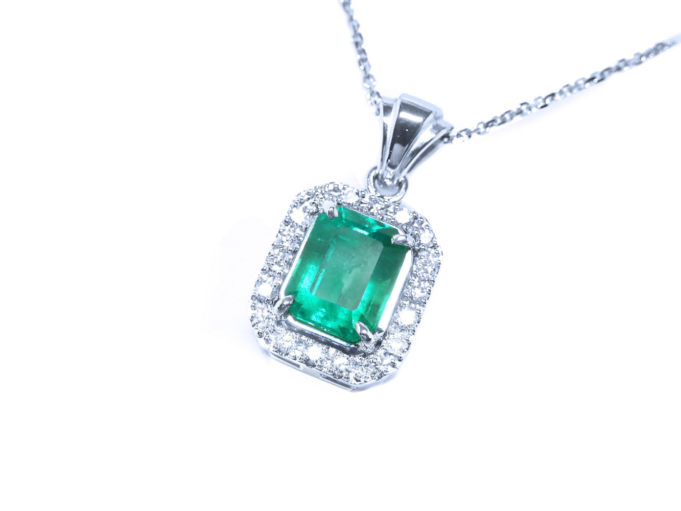 Emerald green gemstone pendant with diamond accents on a left-side position topside view.