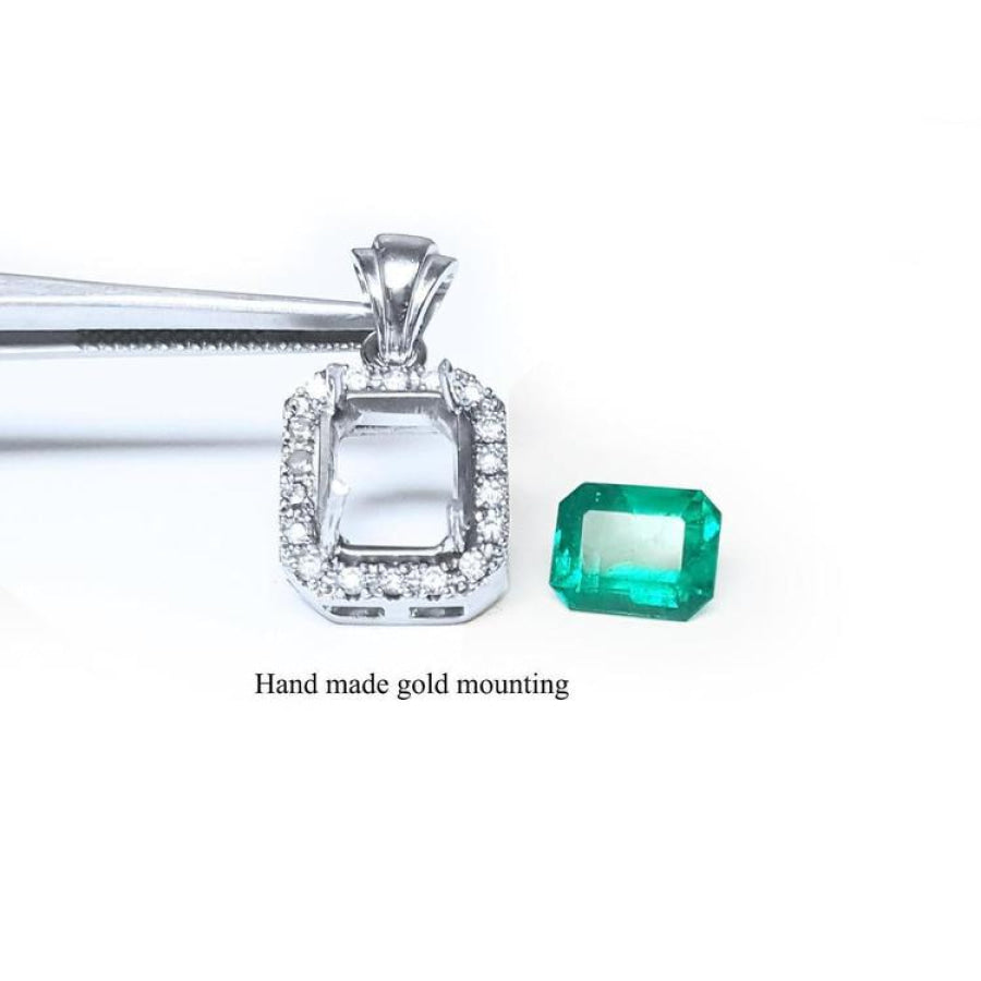 14K white gold halo diamond pendant mounting next to a loose emerald-cut Colombian emerald.
