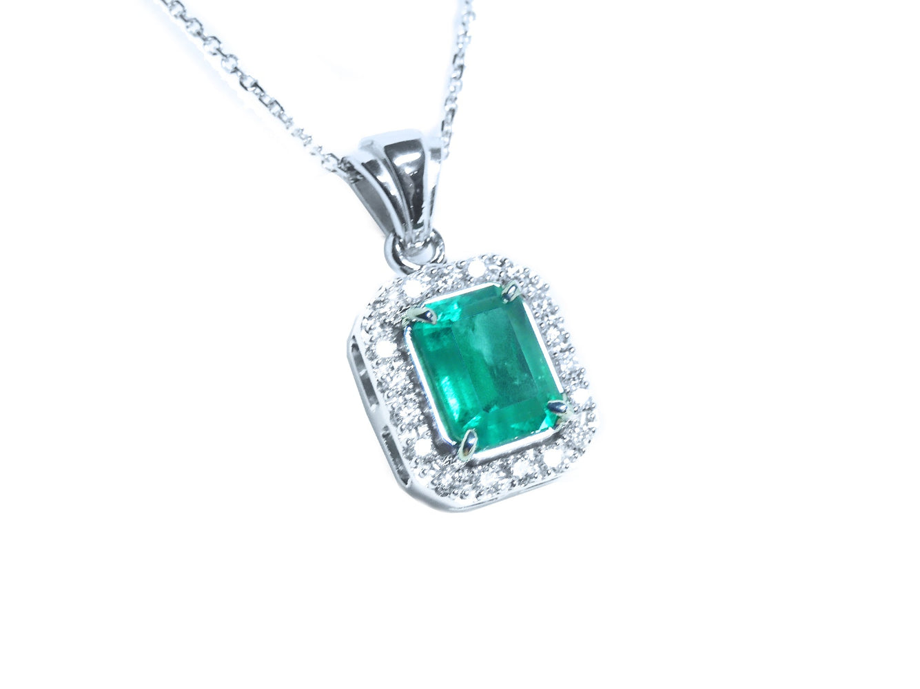 A natural emerald-cut gemstone emerald pendant with a halo diamond accent on a topside view position.