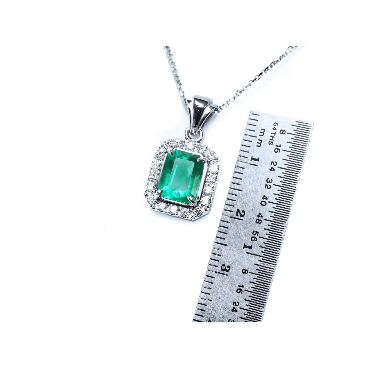 Emerald gemstone pendant on a white gold chain with a ruler for scale on a white background.