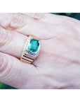 A gold genuine colombian emerald ring being worn by a hand between fingers.
