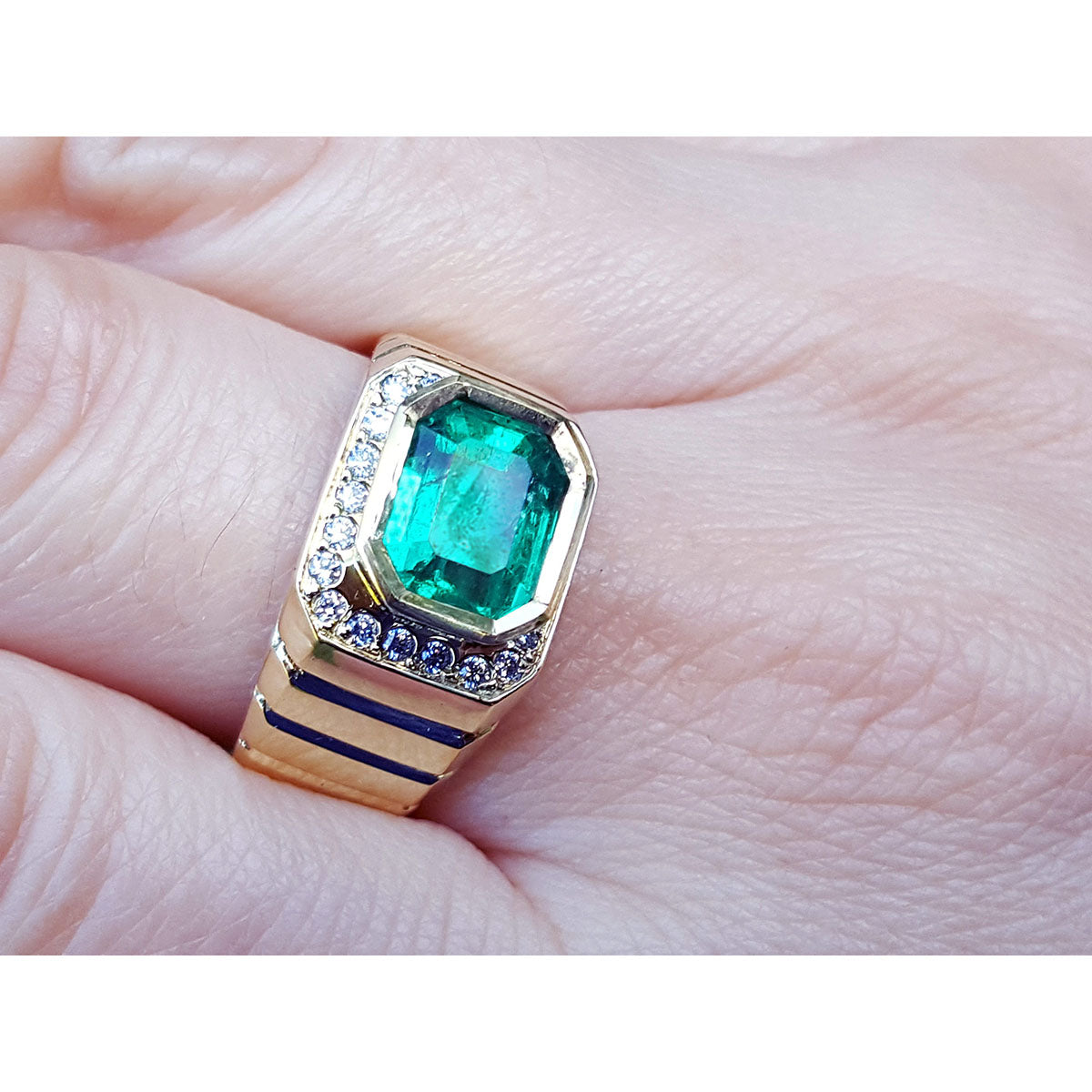 A 18k yellow gold men's emerald ring with accent diamonds on a finger